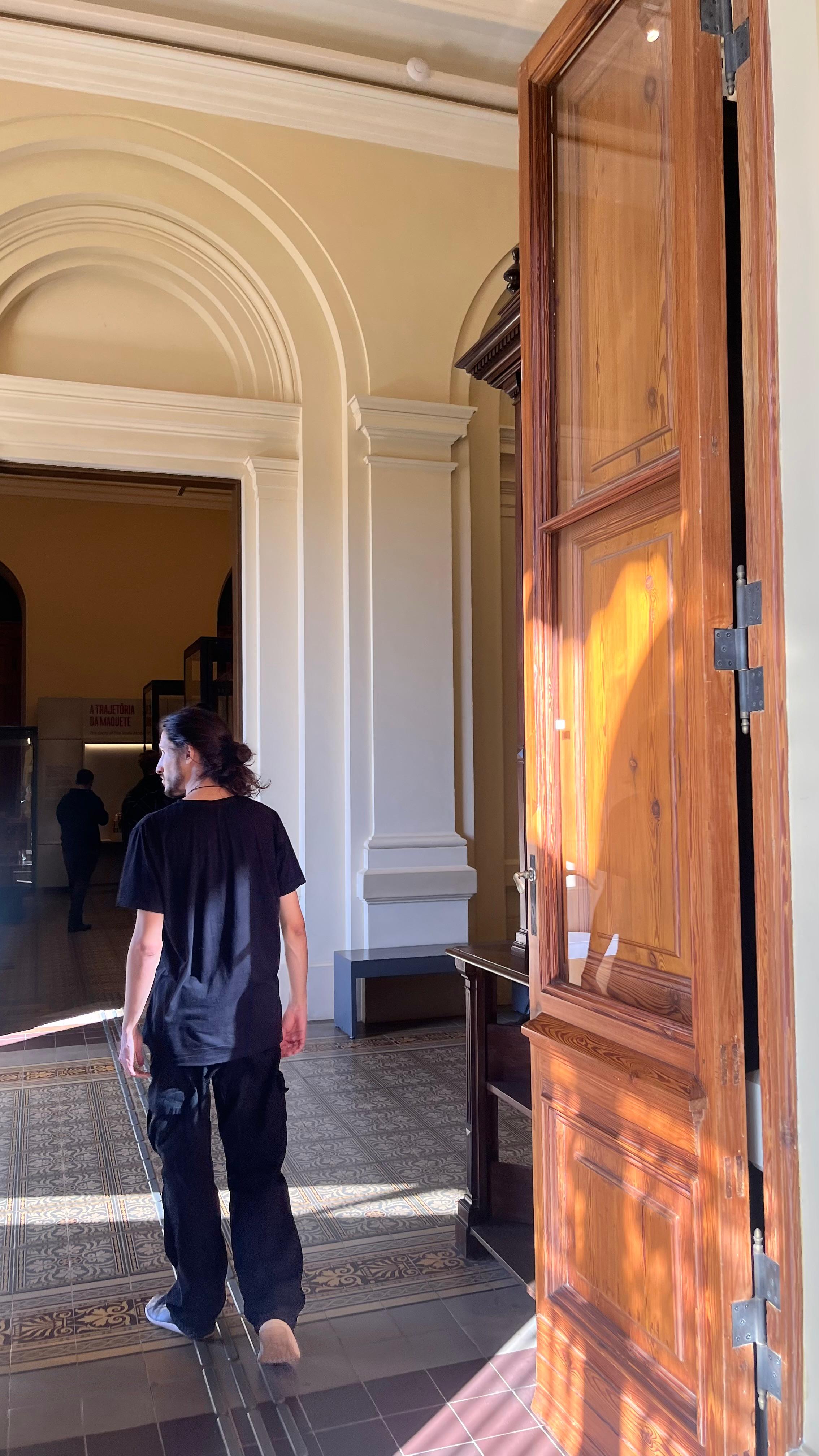 Nyso atravessando um salão de museu iluminado pelo sol.